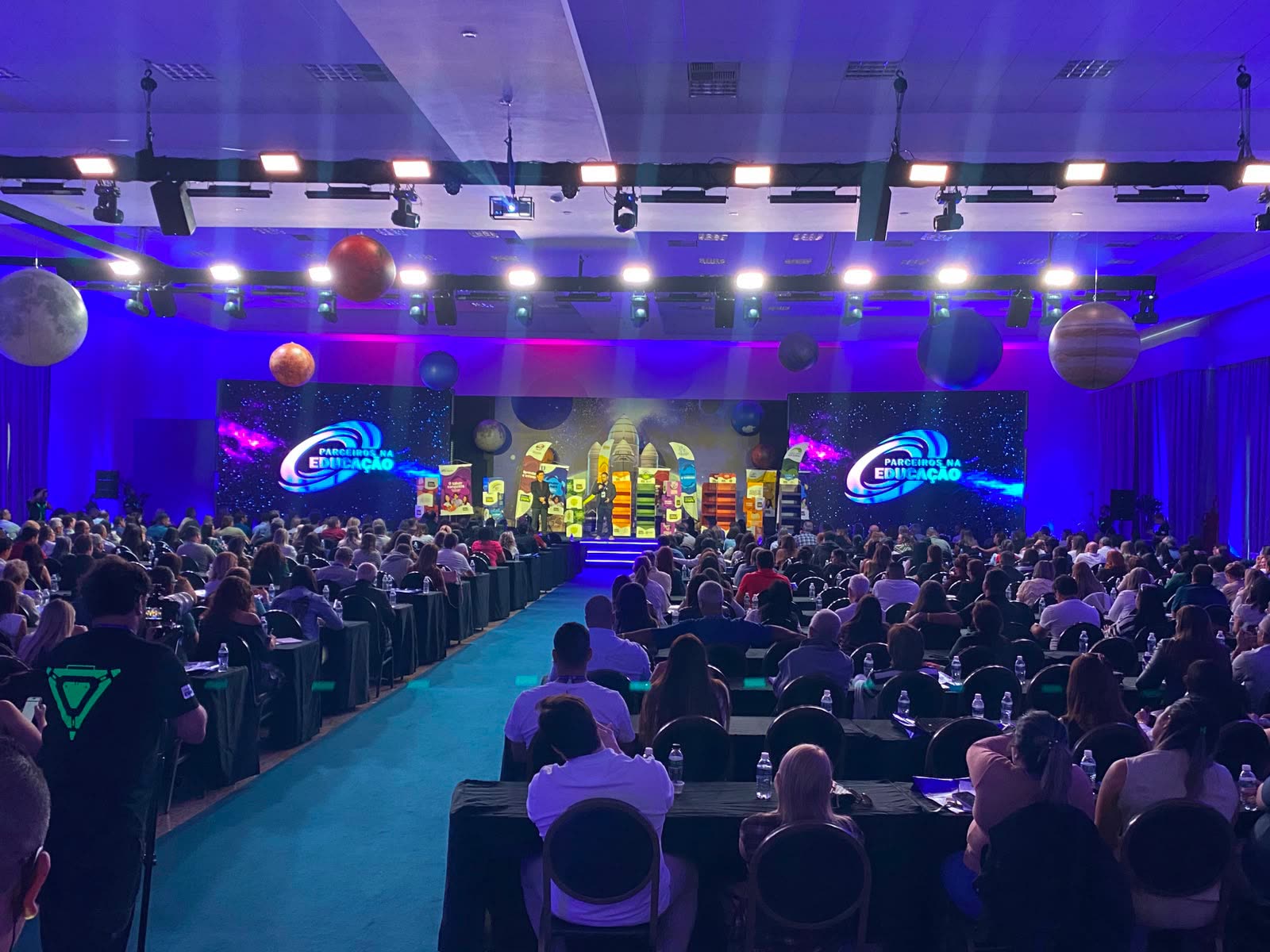 Plateia lotada no evento Parceiros na Educação, com painéis de LED e planetas cenográficos